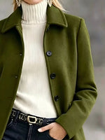 A woman wearing an olive green wool-blend coat over a cream ribbed turtleneck sweater and dark jeans with a black belt.