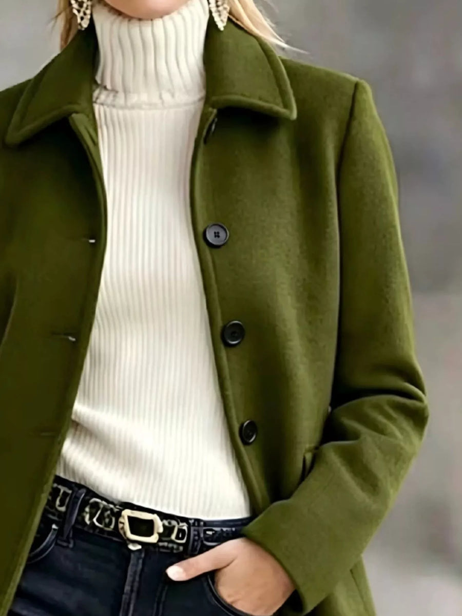 A woman wearing an olive green wool-blend coat over a cream ribbed turtleneck sweater and dark jeans with a black belt.