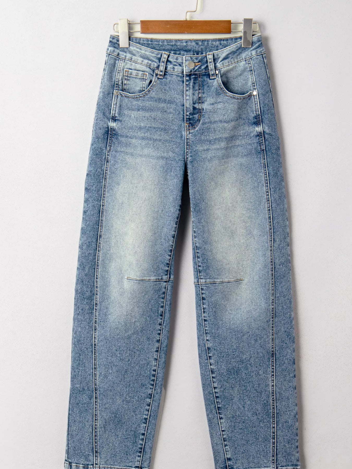 Blue jeans hanging on a wooden hanger against a white background