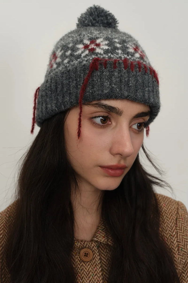 Woman wearing a gray knitted hat with red accents against a white background