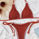 Red textured bikini set on a white surface with sunglasses and a hat.