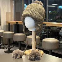 Knitted beanie with pom-poms on a mannequin head in a casual setting.