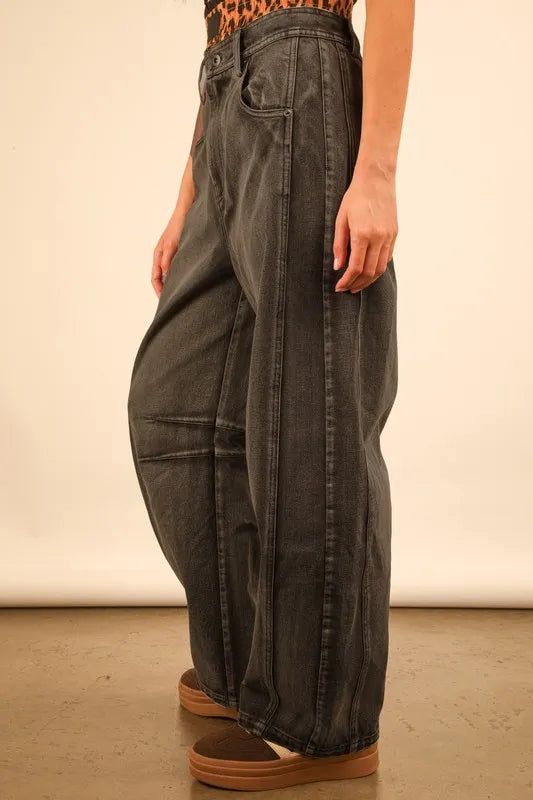Person wearing wide-leg jeans and brown shoes on a plain background