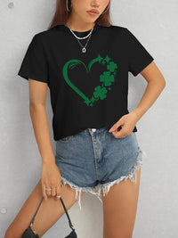 Person wearing a black t-shirt with a green heart and shamrock design, paired with denim shorts.