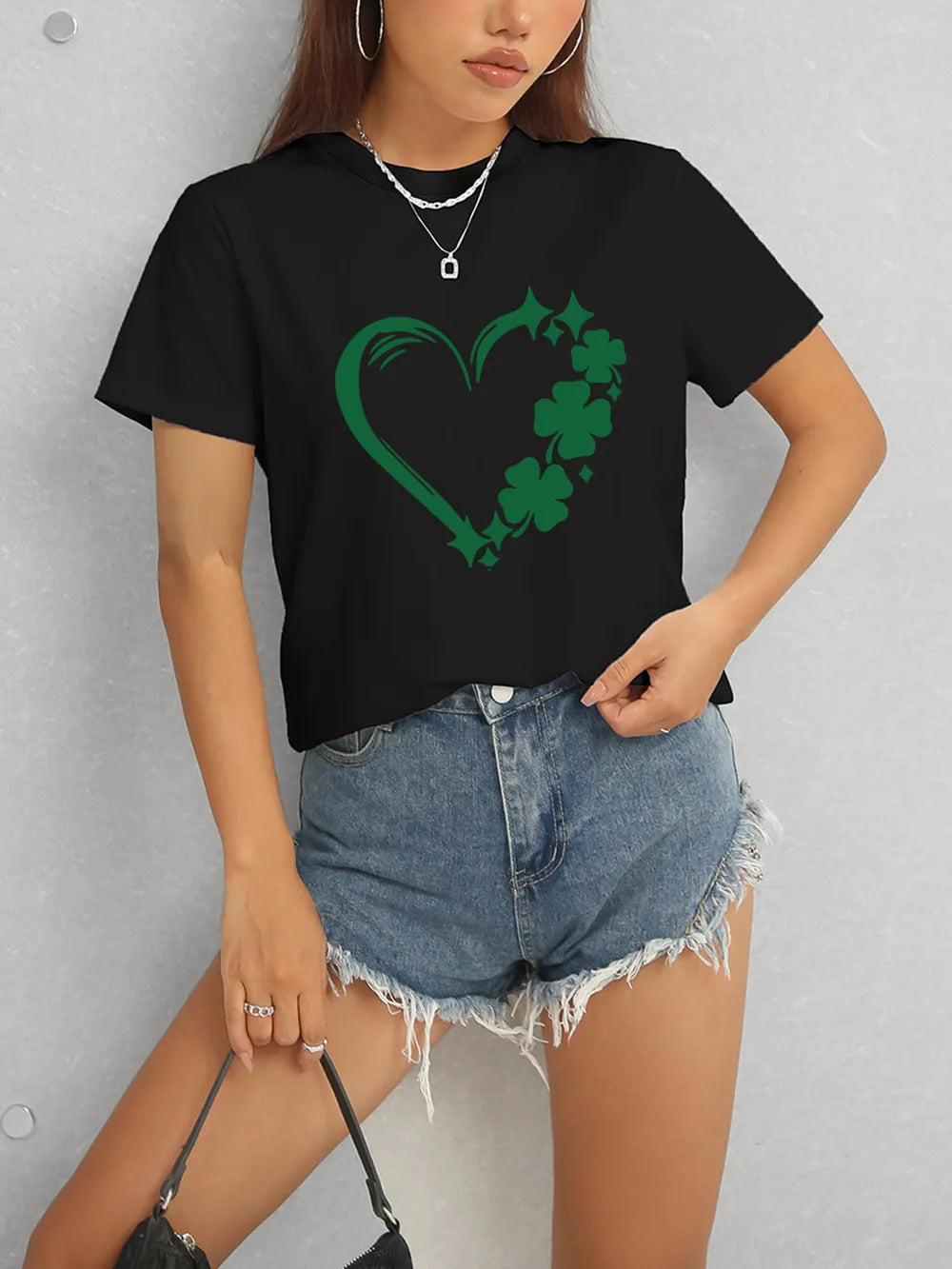 Person wearing a black t-shirt with a green heart and shamrock design, paired with denim shorts.