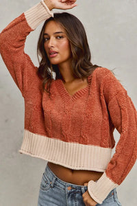 Woman wearing a two-tone sweater with a neutral collar and rust-colored body against a plain background