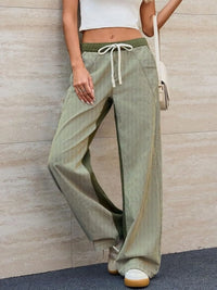 Person wearing green wide-leg pants with a white top against a beige wall.