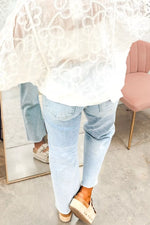 Person wearing light blue jeans and a white lace top in an indoor setting.