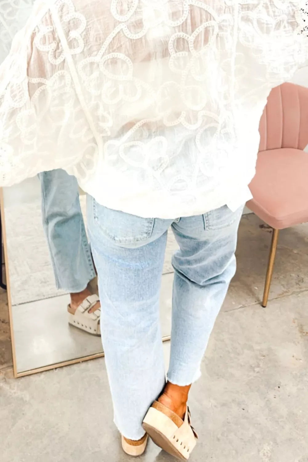 Person wearing light blue jeans and a white lace top in an indoor setting.