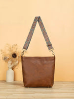 Brown leather handbag with a patterned strap on a wooden surface and beige background