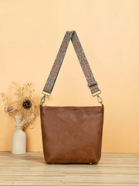 Brown leather handbag with a patterned strap on a wooden surface and beige background