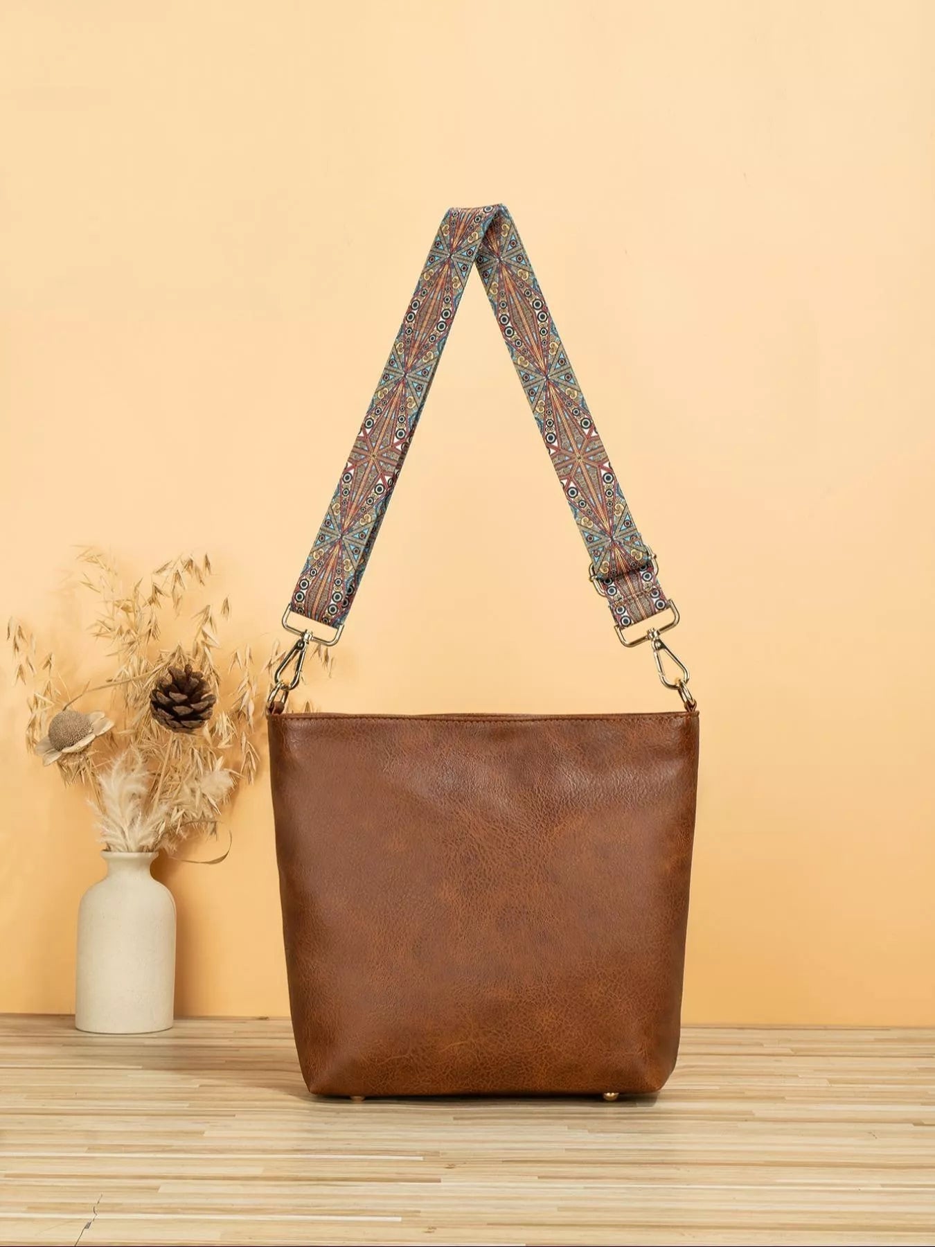 Brown leather handbag with a patterned strap on a wooden surface and beige background