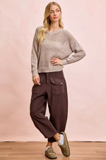 Woman wearing a beige sweater and brown pants against a pink background