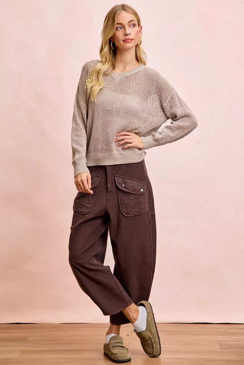 Woman wearing a beige sweater and brown pants against a pink background