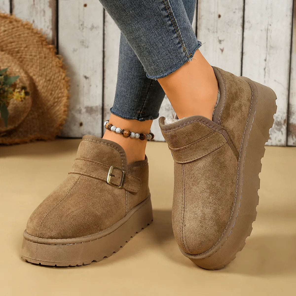 Brown suede loafers worn with jeans on a wooden floor.