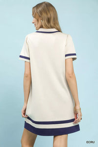 Woman wearing a cream dress with navy trim on a light blue background