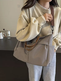 Person wearing a beige sweater and holding a beige bag indoors.