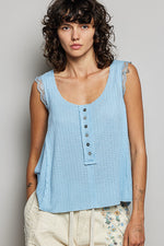 Woman wearing a light blue sleeveless top with buttons against a plain background