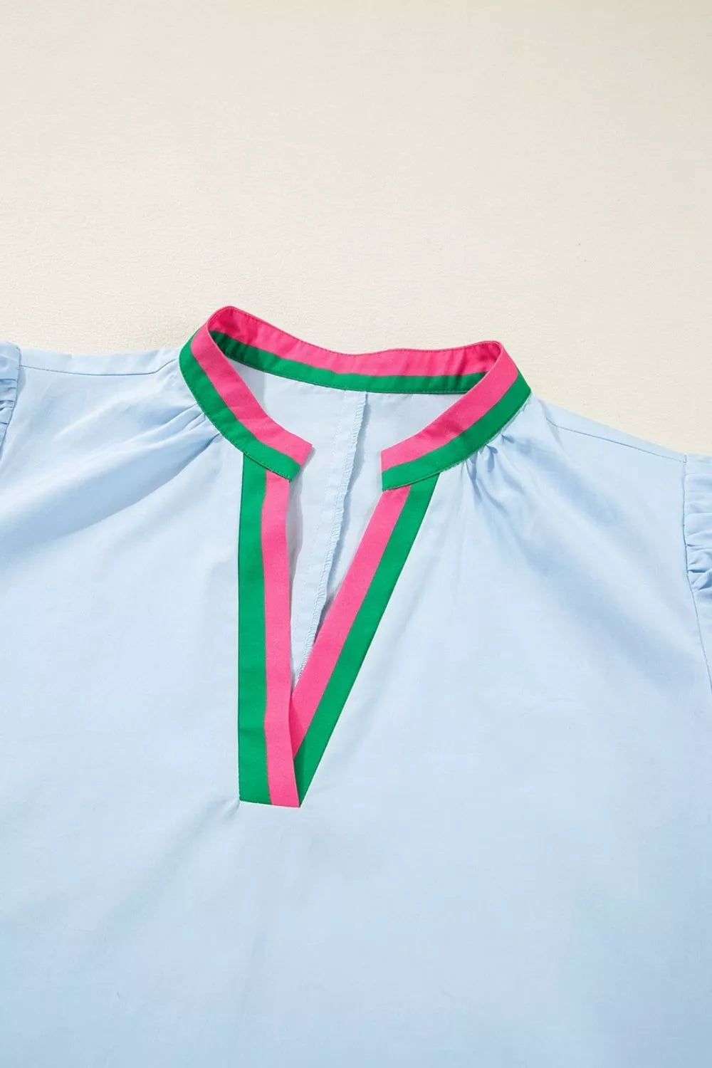 Light blue shirt with green and pink trim on a beige background