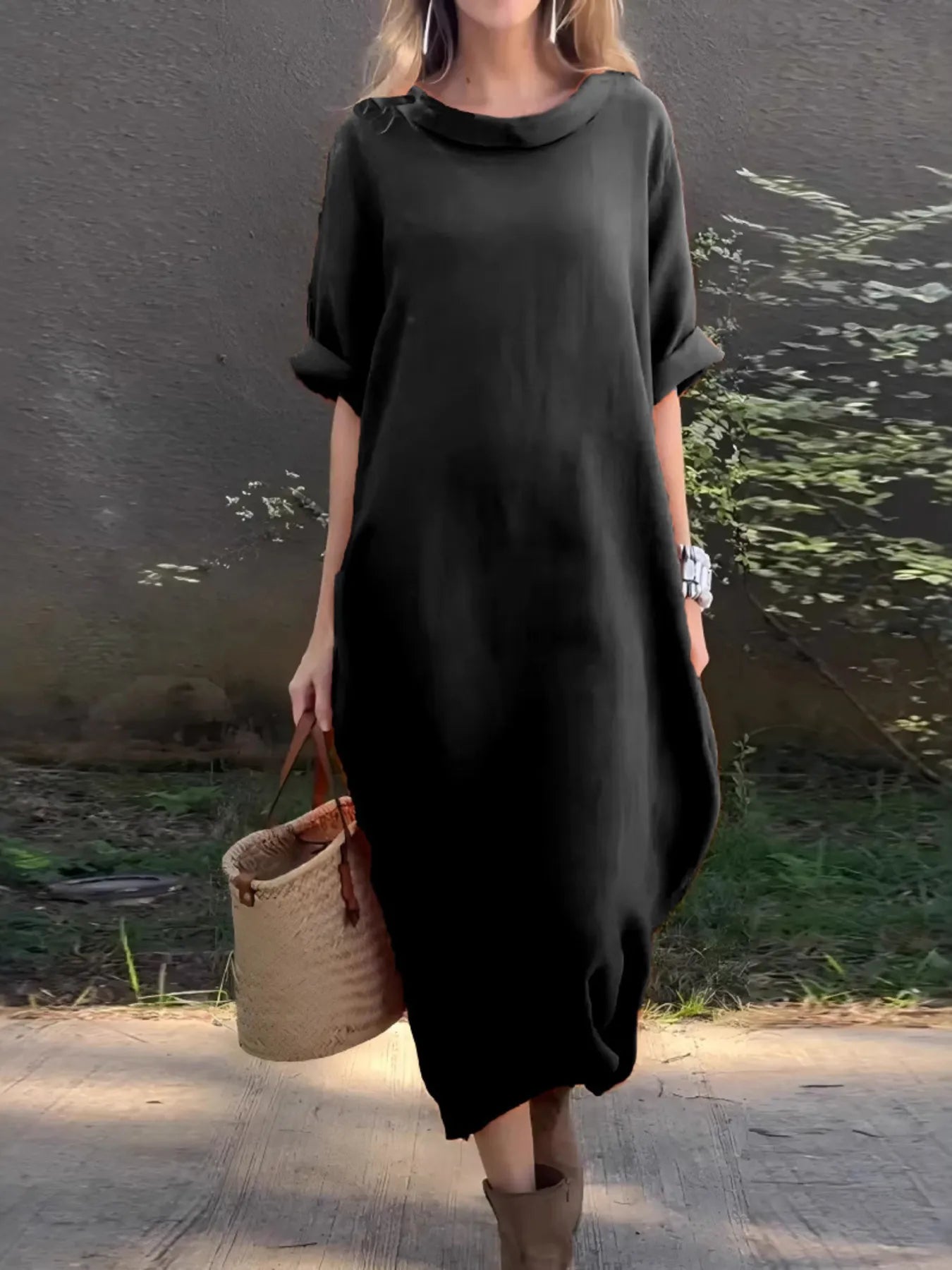 Person wearing a black dress holding a woven basket by a body of water.