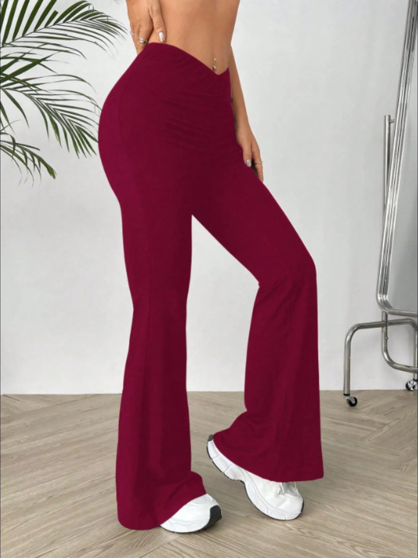 Person wearing burgundy flared pants and white sneakers in a minimal indoor setting.
