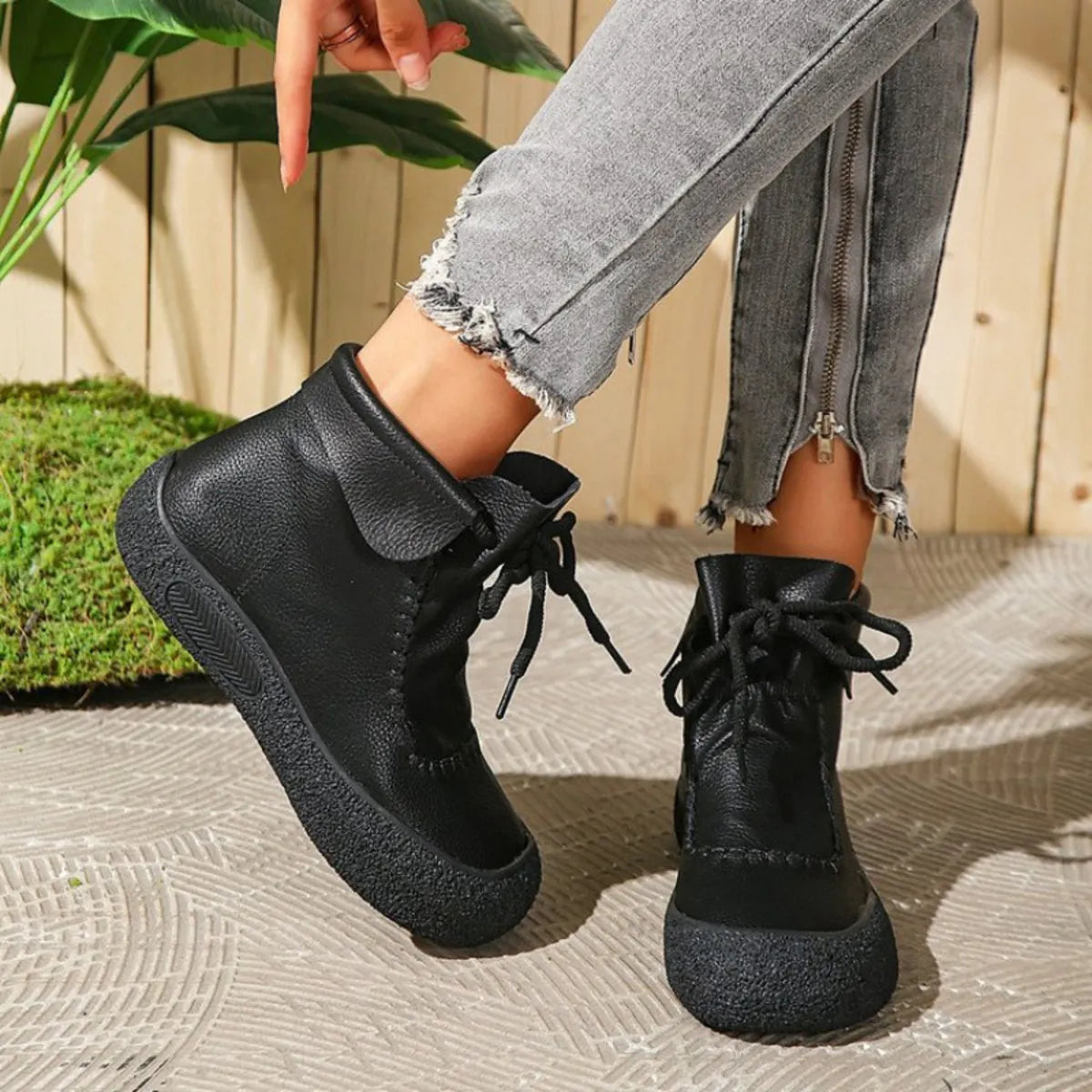 Person wearing black ankle boots with a casual outfit against a wooden fence background