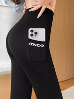 Black high-waisted athletic leggings with a side pocket holding a silver smartphone, featuring the white stylized 'mxc2' logo on the pocket. The model is shown from the waist down in an indoor setting with a light wood door in the background.