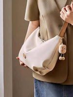 Person holding a beige handbag with a bear charm against a neutral background