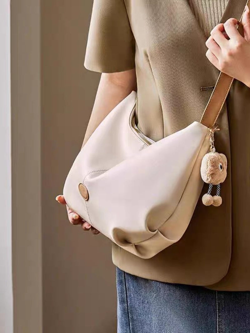 Person holding a beige handbag with a bear charm against a neutral background