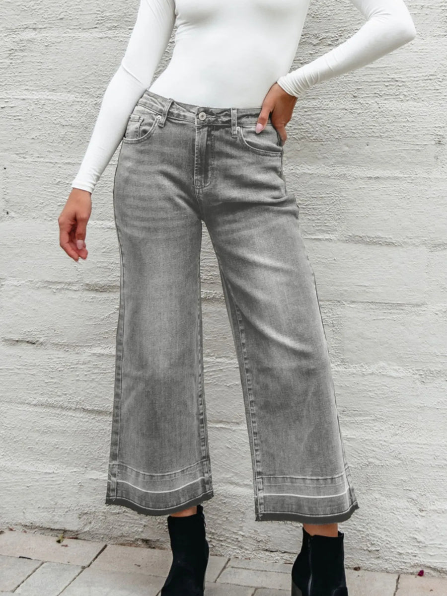 Person wearing gray wide-leg jeans and a white long-sleeve top against a light gray background