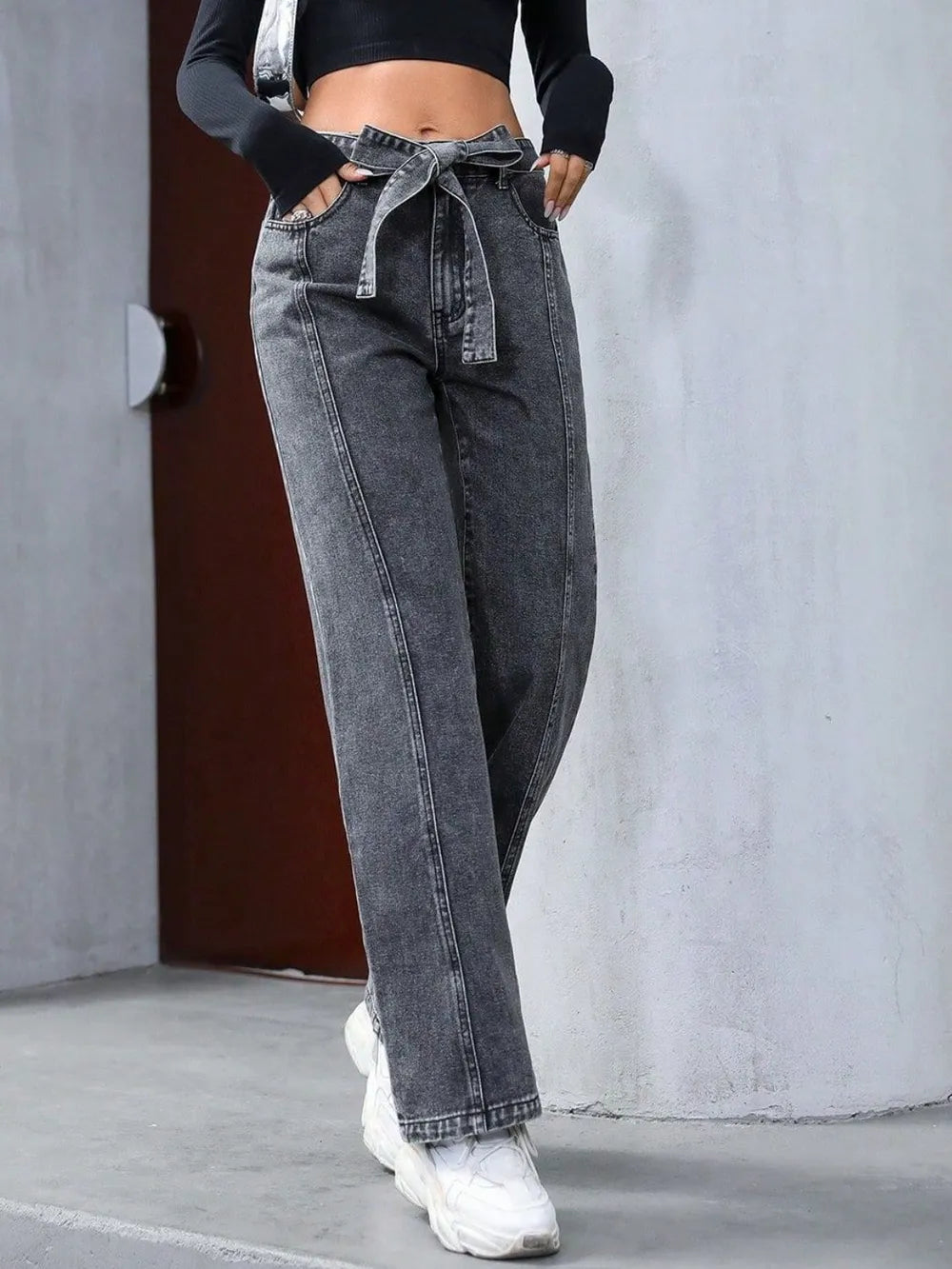 Person wearing high-waisted gray jeans and white sneakers against a neutral background
