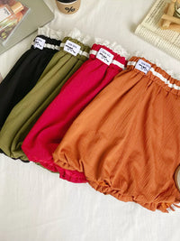Four pairs of colorful bloomers on a white surface with a magazine and cup in the background.
