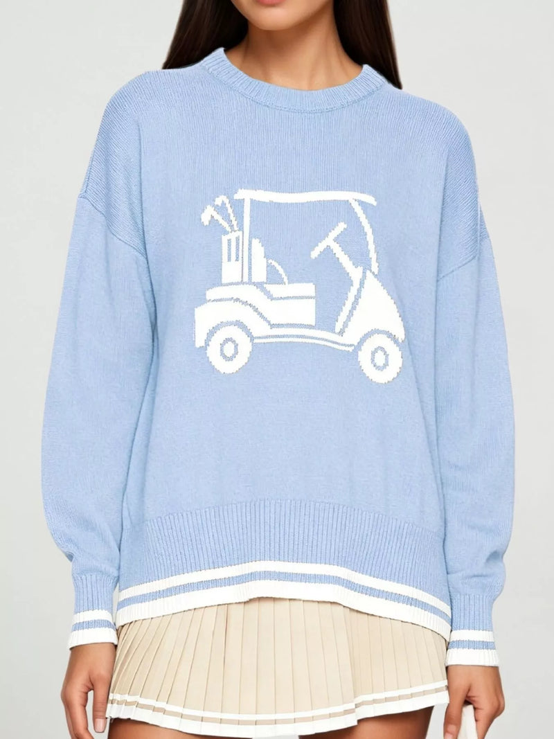 A light blue knit sweater with a white golf cart graphic on the chest, worn by a model with a pleated beige skirt against a light gray studio background.