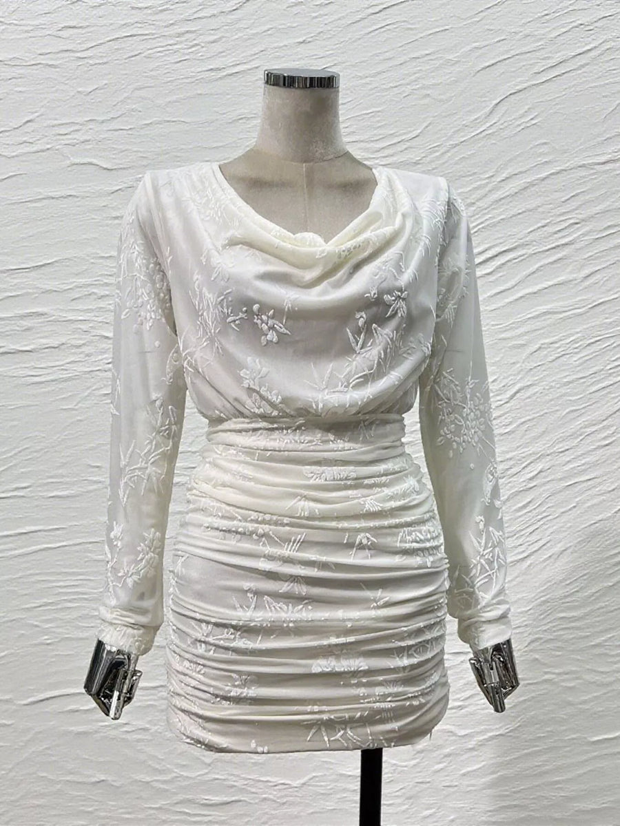 An off-white long-sleeve mini dress with a draped cowl neckline and subtle floral embroidery, displayed on a mannequin against a textured white wall.