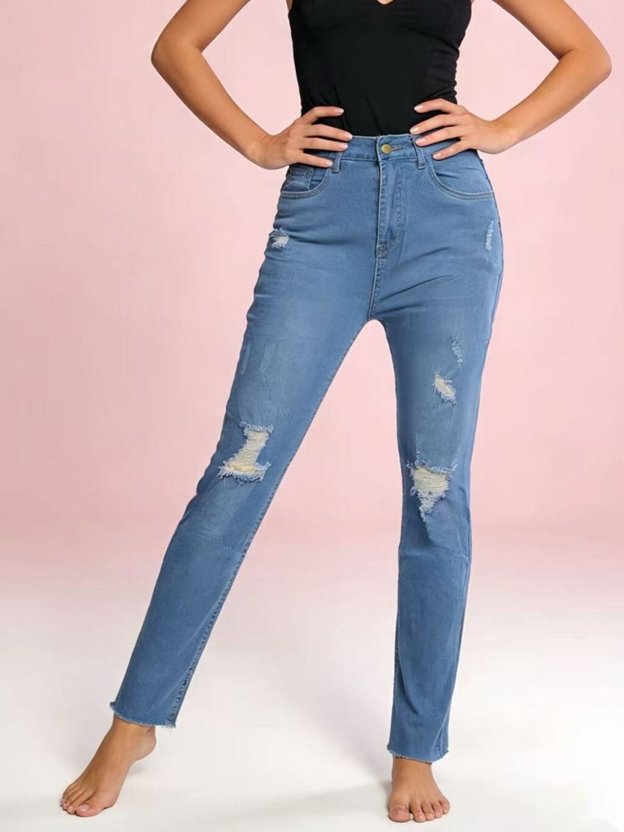 Person wearing blue distressed jeans on a pink background