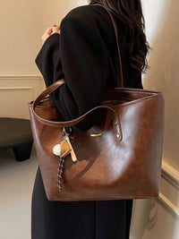 Brown leather tote bag held by a person in a neutral indoor setting