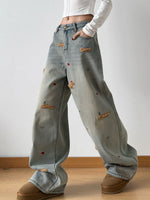 Person wearing light blue jeans with embroidered designs on a plain background