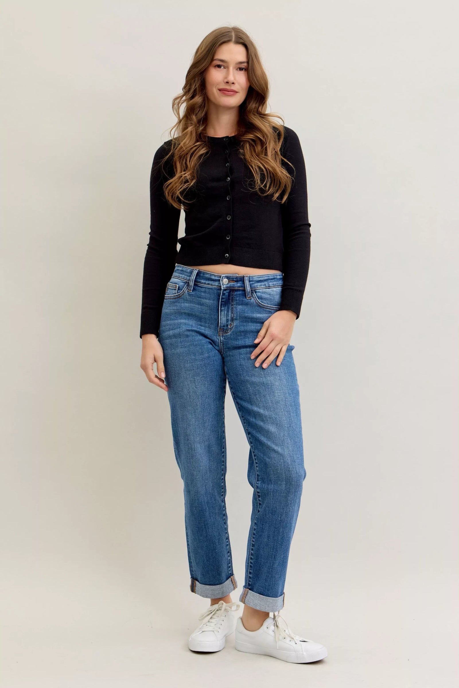 Woman wearing a black cardigan, blue jeans, and white sneakers on a plain background
