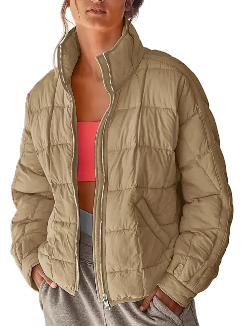 Person wearing a beige puffer jacket over a pink sports bra and gray pants on a white background