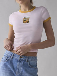 Person wearing a light purple t-shirt with yellow trim and a graphic on a plain background