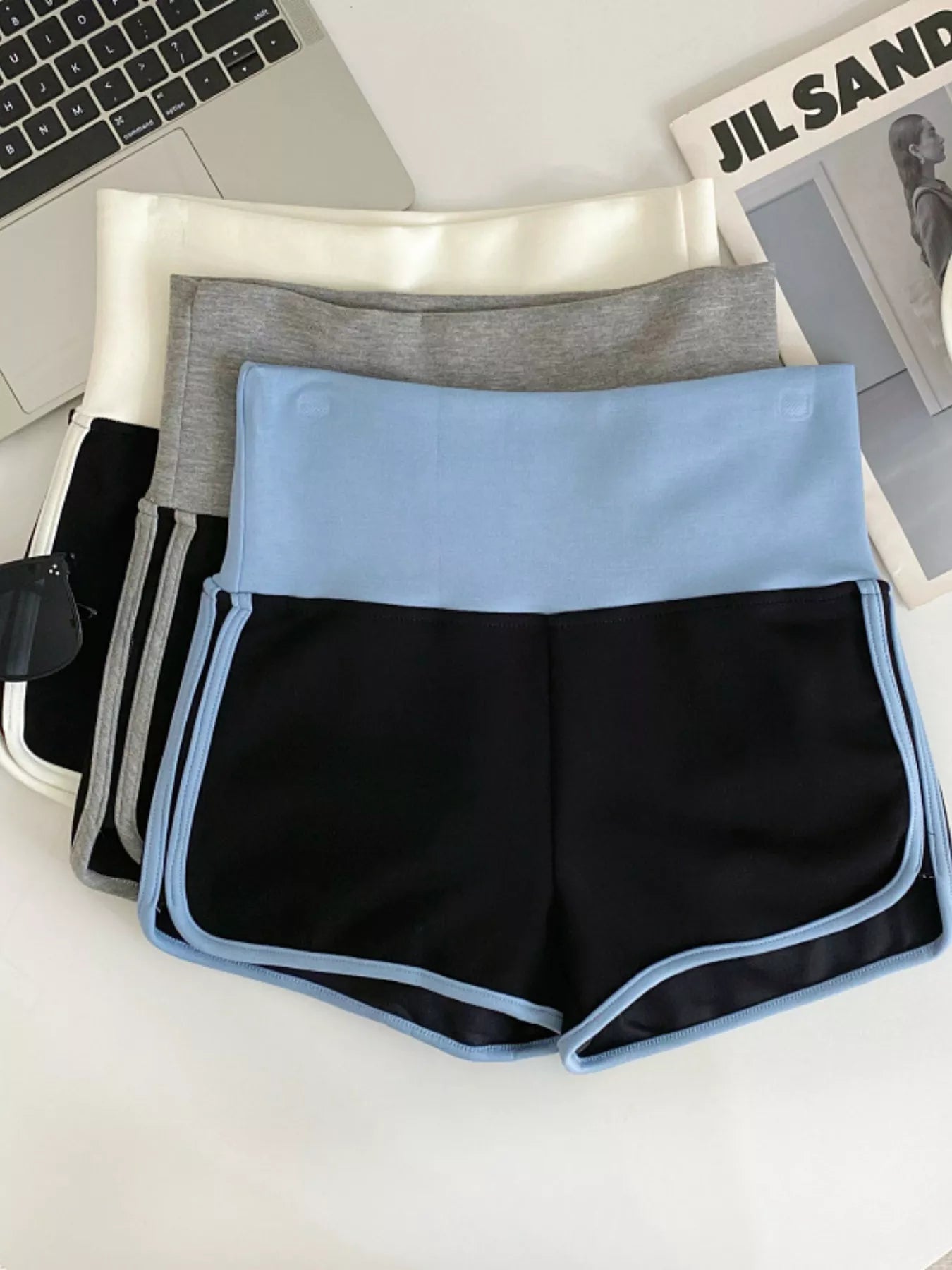 Black and blue athletic shorts on a white surface with a laptop and magazine in the background.