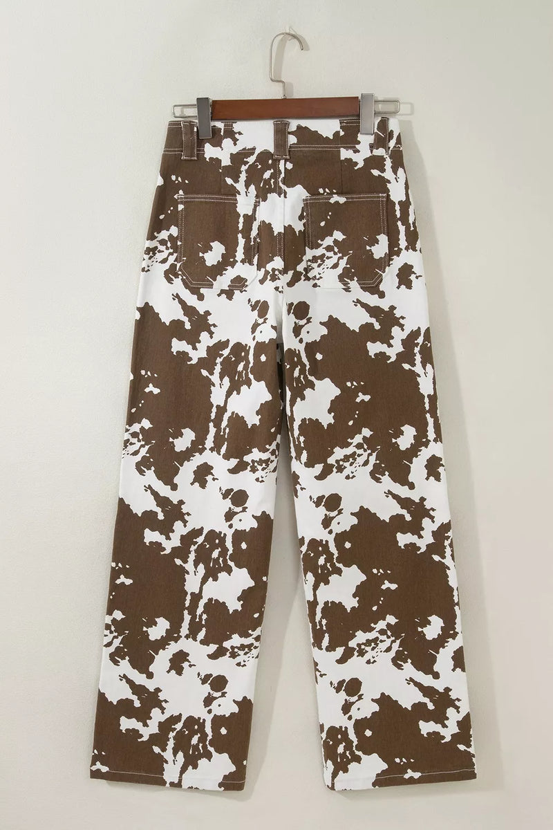 Brown and white abstract patterned pants hanging on a wooden hanger against a plain light beige wall.