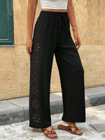 Person wearing black wide-leg pants with a pattern, standing against a beige wall.