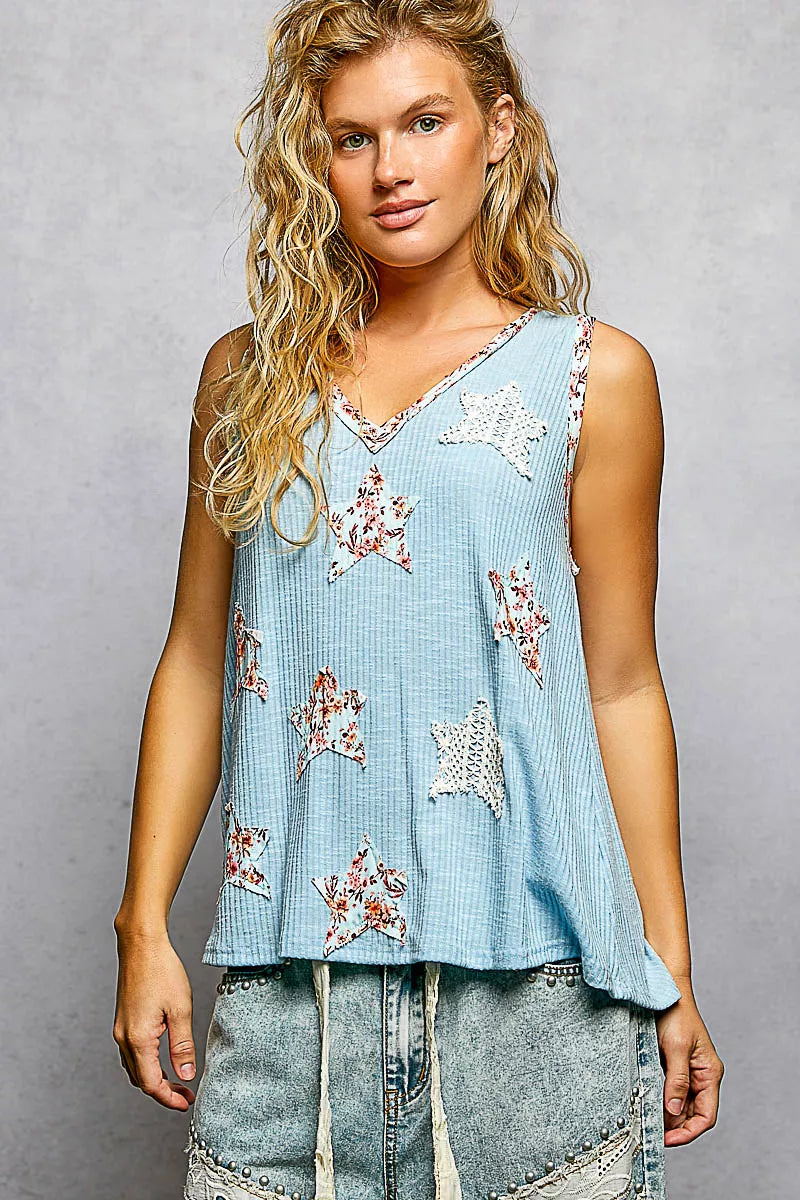 Woman wearing a light blue sleeveless top with floral patterns on a gray background