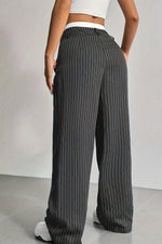 A person wearing dark gray wide-leg pinstripe pants with thin white vertical stripes, paired with a white crop top and white sneakers, shown from the back against a light gray studio background.