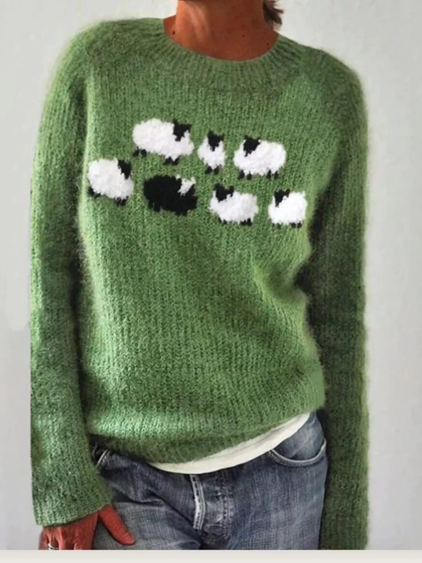 Green sweater with sheep pattern worn by a person against a plain background