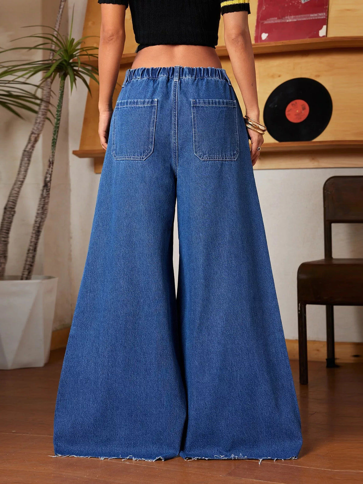 Person wearing blue wide-leg jeans in a room with a plant and record player.