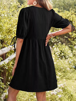 Person wearing a black dress standing in a natural setting with greenery.
