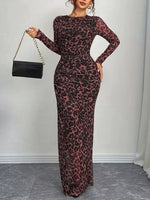 Woman wearing a leopard print dress holding a black handbag against a plain background
