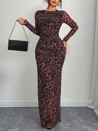 Woman wearing a leopard print dress holding a black handbag against a plain background